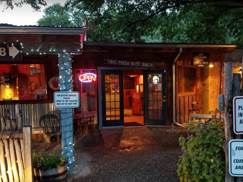 Taos Pizza Out Back entrance lit up at night with a neon open sign