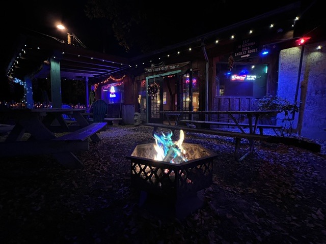Fire pit burning on the Black Jack Smoke Shack patio at night under string lights and neon signs